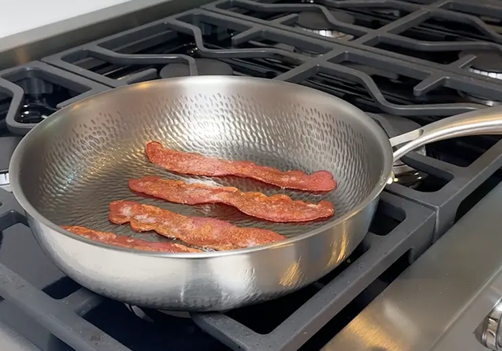 Bacon frying in Alex J.'s Plateful titanium pan on a gas stovetop